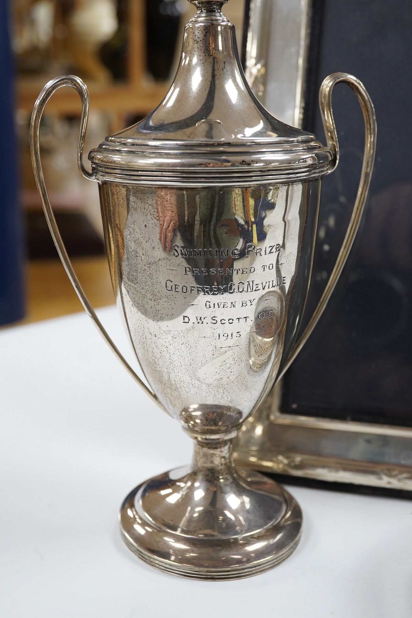 A George V silver two handled presentation trophy cup, 21.8cm, a modern silver wine coaster, a modern mounted silver photograph frame and a George V silver mounted photograph frame. Condition - poor to fair